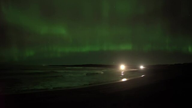 Headlights on beach driving under aurora borealis Iceland