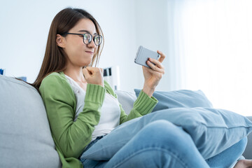 Asian woman wear eyeglasses play mobile game on smartphone at home. 