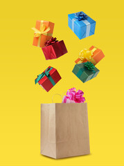 Many different gift boxes falling into paper shopping bag on yellow background