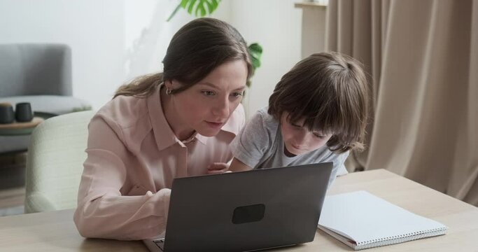 Mom and son are shopping together online using laptop, choosing new toys and gifts. Cute boy whispers his secrets in his ear, trusting his parents. Online schooling learning at home.