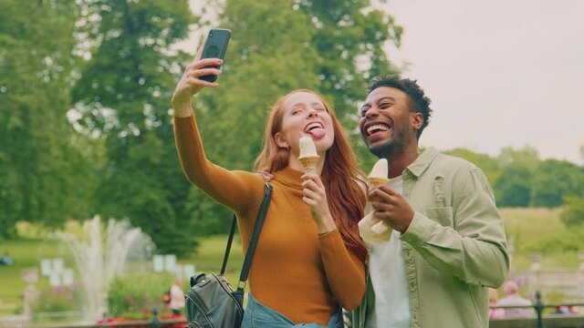 Young couple travelling through city park eating ice cream together posing for picture for social media- shot in slow motion