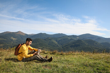 Naklejka na ściany i meble Tourist with thermos and backpack enjoying beautiful mountain landscape