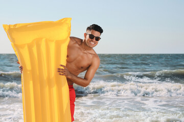 Man with yellow inflatable mattress at beach - obrazy, fototapety, plakaty