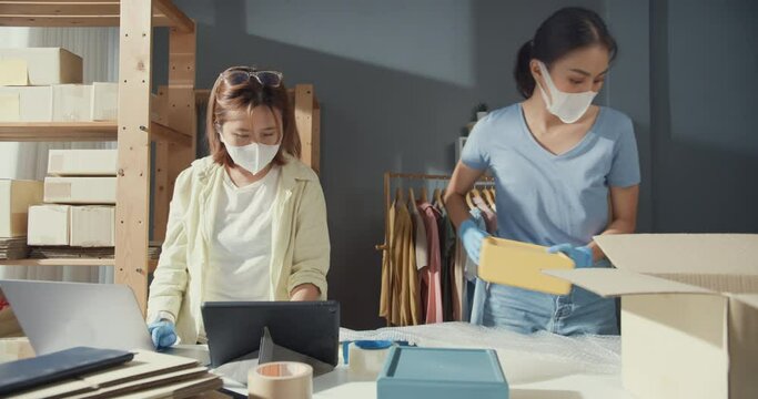 Professional two Asian lady with casual wear protection glove surgical mask check stock inventory system prepare packing order shirt product sent customer. New business opportunity after the COVID-19.