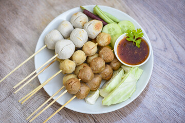 Meatballs on skewers on white plate and fresh vegetables cabbage yard long bean cucumber, Asian Thai food grilled meatballs fishball and porkball with picy sauce