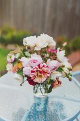 bunch of rose flowers in vase on top of outdoor table in sunny backyard
