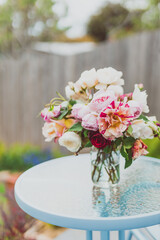 bunch of rose flowers in vase on top of outdoor table in sunny backyard