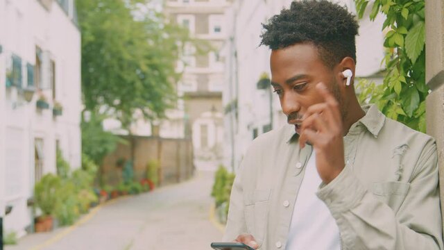 Young man travelling through city listening to music on wireless earbuds on mobile phone - shot in slow motion