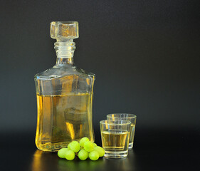 Grappa, strong alcohol in a glass decanter and glasses on a black background, next to a bunch of...
