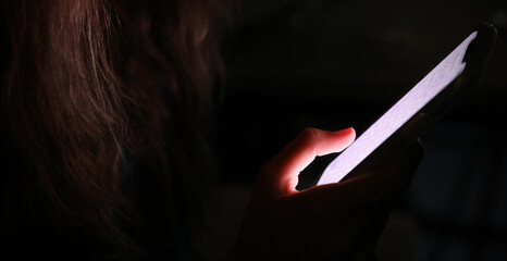 Anonymous female using a mobile cell phone at night in the dark. The glow of the screen...