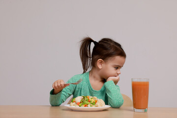 Cute little girl refusing to eat vegetable salad at table on grey background