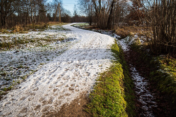 A winding walking trail with the first snow and footprints on sunny autumn day. Kuldiga, Latvia