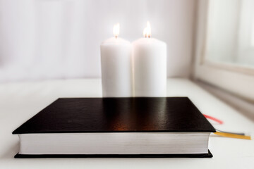 two lighted candles and a black-bound book by the window. Selective focus.
religiosity and reading religious books.
