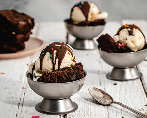 Vanilla ice cream sundae with hot fudge and brownies on a picnic table 