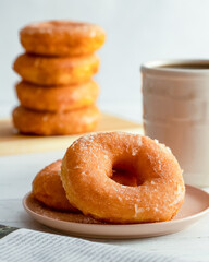 A plate of sugar donuts and coffee, with a stack of sugar donuts in the background