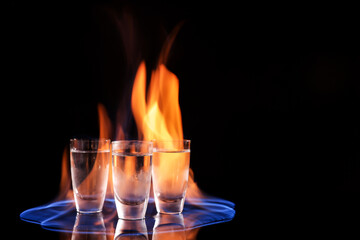 Vodka in shot glasses and flame on black background, space for text