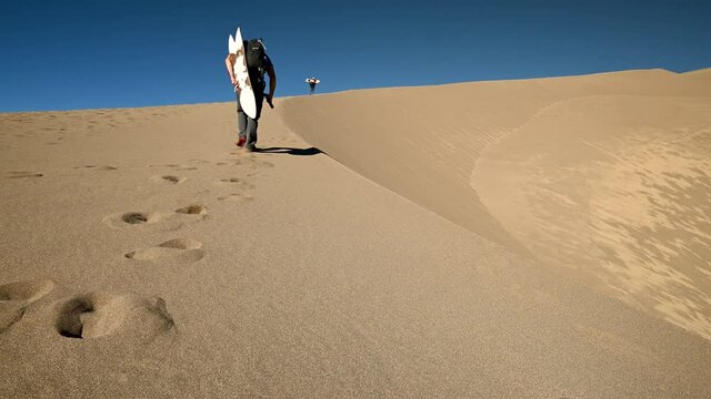 Hiker with sandboard walking along a sand dune ridge in Great Sand Dunes National Park, Colorado