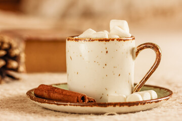 A mug of hot coffee , hot chocolate,  cocoa with marshmallows , a book on beige background. Hot cocoa, coffee, chocolate , cinnamon sticks and marshmallow on a cold day.