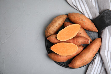 Slate board with cut and whole sweet potatoes on light grey table, top view. Space for text