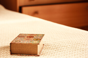 A book in a colorful cover on the knitted blanket on the bed in the bedroom, copy space