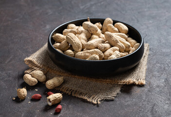 unpeeled peanuts in a black bowl on a dark texture  background. Macro and close up image