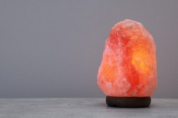 Himalayan salt lamp on stone table near light grey wall, space for text - obrazy, fototapety, plakaty