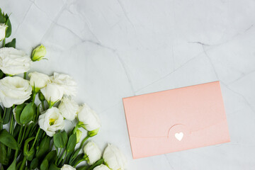White roses with pink envelope over the marble background. 