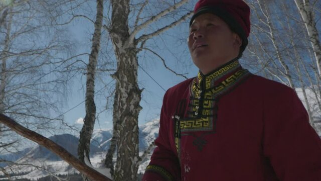 Two men dressed in traditional Mongolian clothing hiking in a forest in winter