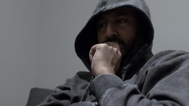 An Indian man wearing a hoodie with a clutched hand covering his face, the man in a dark psychological space as he works through the problems in his mind