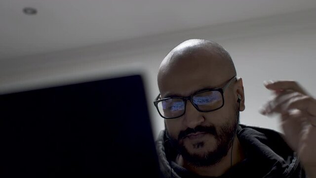 An Indian Corporate Employee Taking His Headphones Out Of His Ears After Waving Goodbye And Signing Off From An Online Conference Call, Casually Dressed As He Continues To Work Remotely From Home