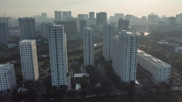 Drone clockwise hyperlapse orbit around large multi-tower residential apartment complex or condominium on sunny early morning with green space panorama of city and highway