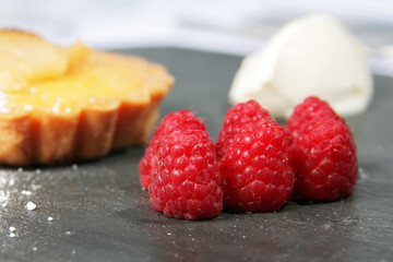 raspberries on a slate bed with cream and tart in background differential focus
