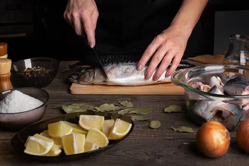 Foto op Canvas Cooking fish, salting mackerel, female hands carving fish, in the foreground spices, salt, pepper, lemon, bay leaf. Home cooking concept © Ольга Рязанцева