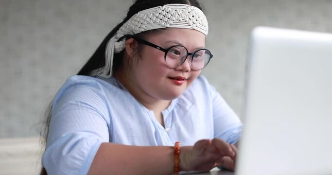 Cheerful girl with down syndrome typing on netbook and chatting with friends on social media while entertaining at weekend at home