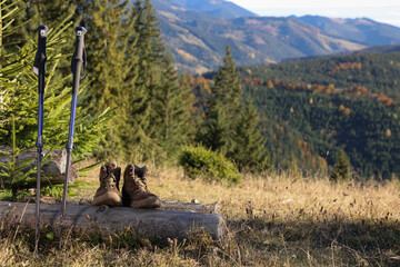 Pair of trekking poles and hiking boots in mountains on sunny day, space for text