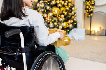 little girl in a wheelchair near the Christmas tree. disabled person holding yellow, golden New...