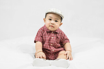 Cute 6-7 months little asian baby boy in casual outfit and hat sitting on white blanket cool and happily at home,Stylish fashionable kid. Adorable child in fashion and Style