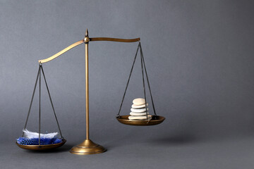 Scales with stones and feathers on grey background, space for text. Balance concept