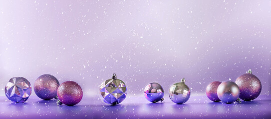 Pink and purple Christmas tree bulbs on purple background with falling snow, banner size