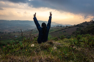young girl in victory pose at mountain top with hill range background and dramatic sky at morning