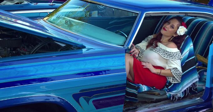 Young Latino Mexican fashionable model girl with lipstick and earrings relaxing in classic vintage car in Los Angeles, California, 4K