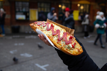 Female hand holding delicious sandwich called Zapiekanka. Okrąglak street food court on Plac Nowy...