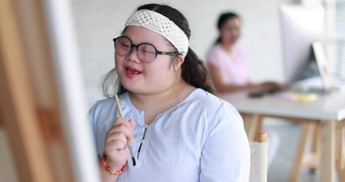 Positive girl with down syndrome singing song while sitting near easel with brush during art lesson and enjoying painting