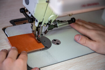 Close up craftsman hands sew stuff blank for wallet use sewing machine. Working at leather workshop