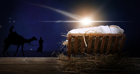 Wooden manger with dummy of baby on table at night. Concept of Christmas story