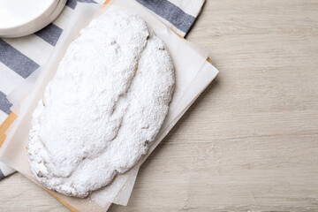 Delicious Stollen sprinkled with powdered sugar on wooden table, top view. Space for text