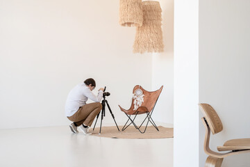 Male photographer working in minimal light and airy interior , white and beige chair, rug and pillows