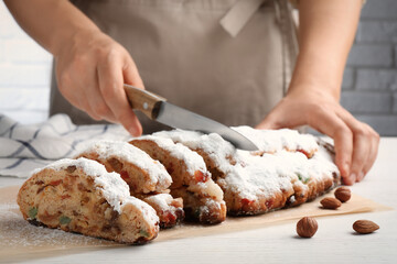 Woman cutting traditional Christmas Stollen with icing sugar at white wooden table, closeup