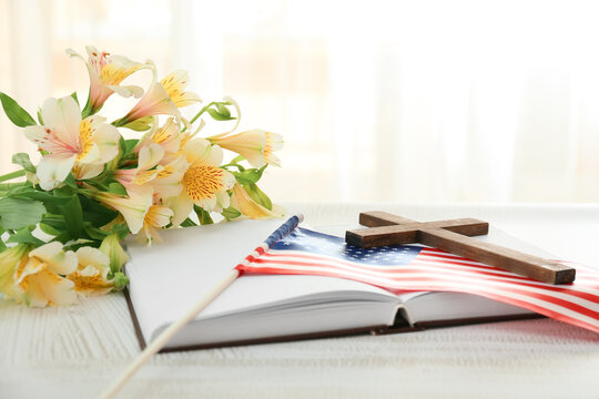 Holy Bible with cross, flowers and USA flag on table in room