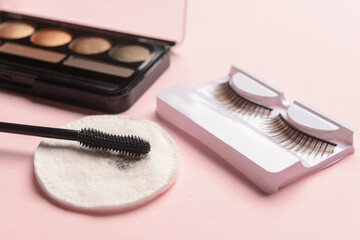 Eyeshadows, mascara, false eyelashes and used cotton pad on pink background, closeup